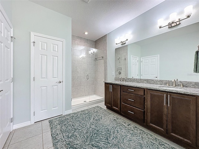 bathroom featuring double vanity, a sink, tile patterned flooring, a shower stall, and a textured ceiling