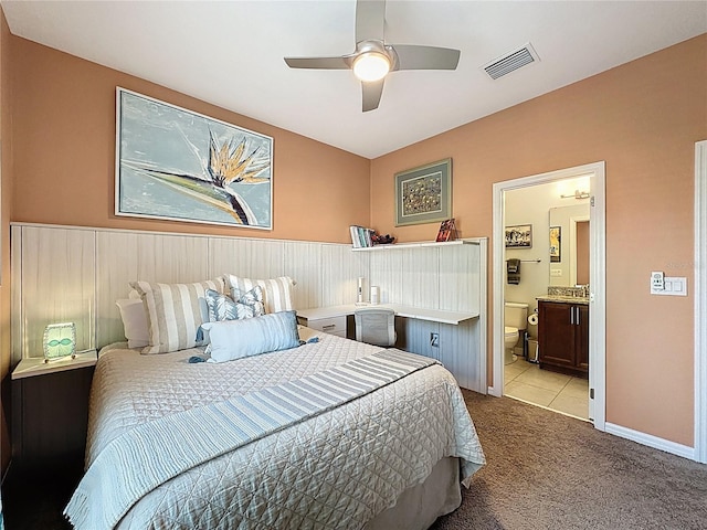 bedroom with a ceiling fan, visible vents, baseboards, ensuite bath, and light colored carpet