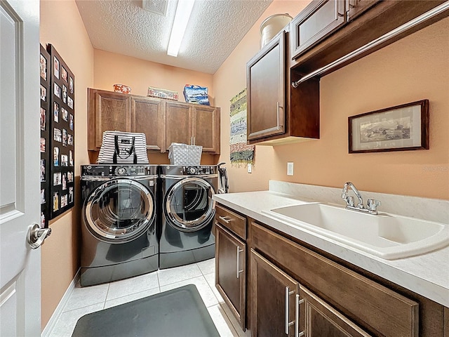 washroom with a sink, a textured ceiling, washing machine and dryer, cabinet space, and light tile patterned floors