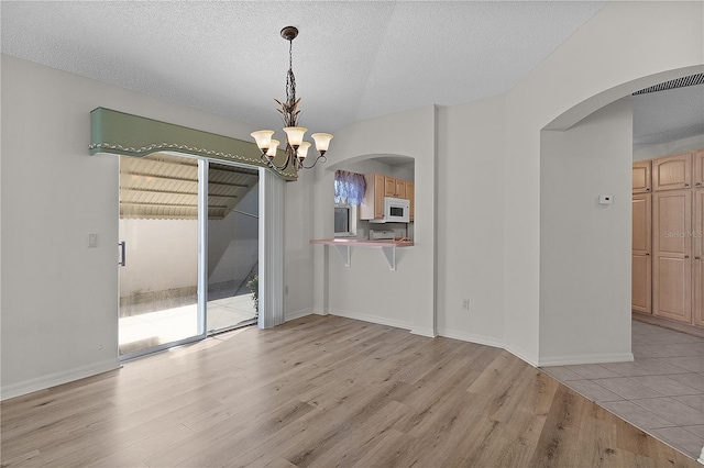 1135 Santa Cruz Dr, The Villages, FL 32162 - unfurnished dining area with an inviting chandelier, light wood-style flooring, arched walkways, and a textured ceiling
