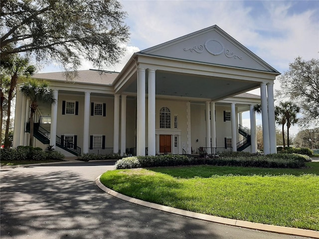 greek revival inspired property featuring a front lawn, stairway, curved driveway, and stucco siding