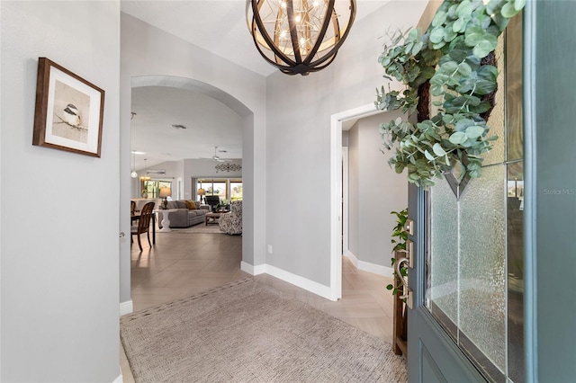 foyer with baseboards, arched walkways, a notable chandelier, and vaulted ceiling