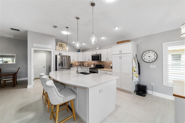 kitchen featuring visible vents, vaulted ceiling, stainless steel appliances, white cabinetry, and a sink