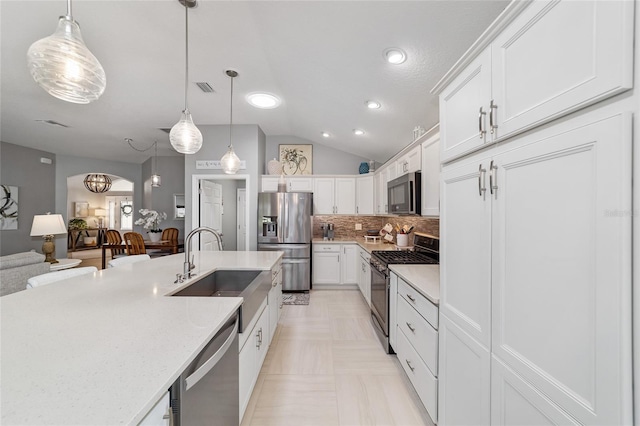 kitchen with arched walkways, a sink, stainless steel appliances, vaulted ceiling, and backsplash