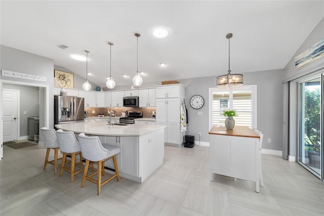 kitchen featuring visible vents, a spacious island, a sink, stainless steel appliances, and vaulted ceiling