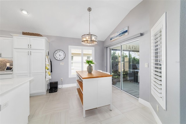 kitchen featuring baseboards, butcher block counters, vaulted ceiling, hanging light fixtures, and white cabinetry