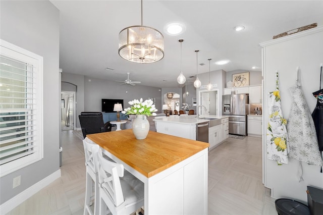 kitchen with open floor plan, an island with sink, stainless steel appliances, arched walkways, and white cabinetry