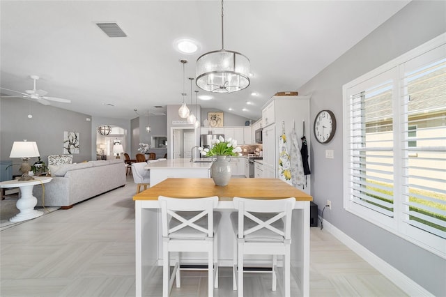 dining area featuring visible vents, ceiling fan with notable chandelier, baseboards, and vaulted ceiling