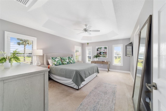 bedroom with visible vents, baseboards, a tray ceiling, ceiling fan, and light carpet