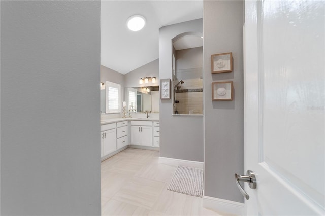 bathroom with vanity, lofted ceiling, a walk in shower, and baseboards