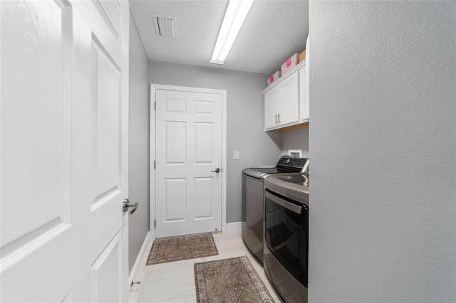 laundry area with visible vents, a textured ceiling, cabinet space, separate washer and dryer, and baseboards