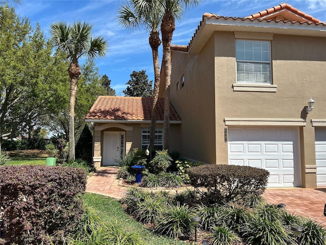 view of front of house featuring a tiled roof, an attached garage, driveway, and stucco siding