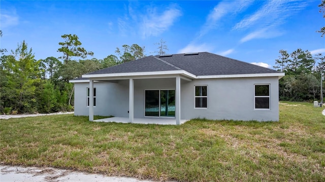 rear view of property featuring a yard, stucco siding, a patio, and roof with shingles