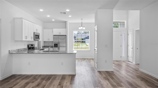 kitchen featuring light stone counters, visible vents, a peninsula, white cabinets, and appliances with stainless steel finishes