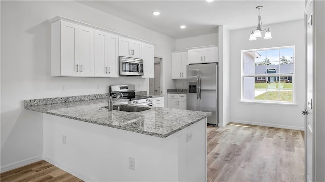 kitchen featuring light stone counters, appliances with stainless steel finishes, a peninsula, white cabinetry, and a sink