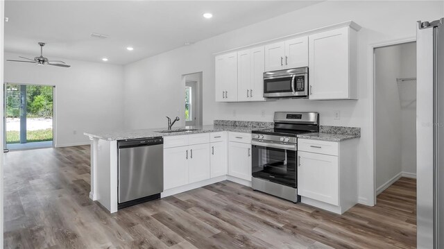 kitchen with recessed lighting, appliances with stainless steel finishes, a peninsula, white cabinetry, and a sink