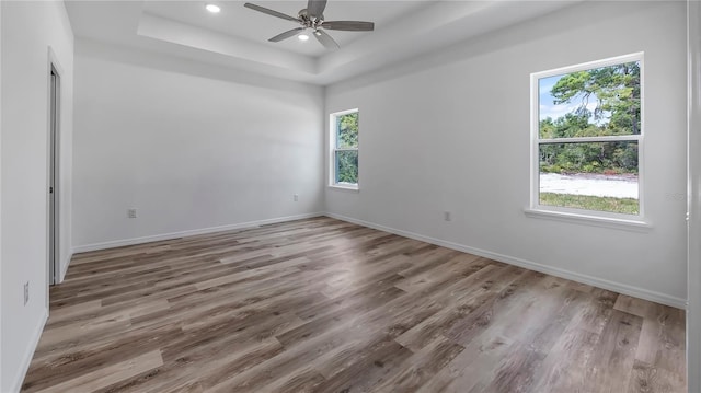 empty room with recessed lighting, a tray ceiling, baseboards, and wood finished floors