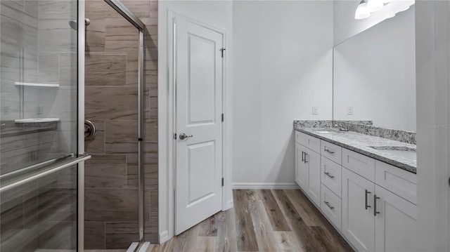 bathroom featuring baseboards, double vanity, a stall shower, wood finished floors, and a sink