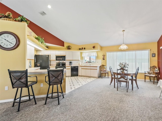 kitchen featuring a peninsula, lofted ceiling, black appliances, light countertops, and light colored carpet