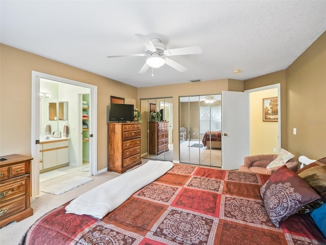 bedroom featuring visible vents, two closets, ensuite bath, light colored carpet, and ceiling fan