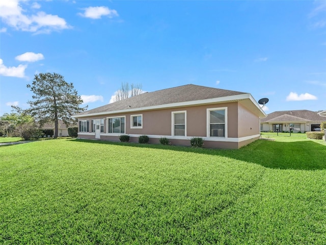 back of property with stucco siding, a yard, and roof with shingles