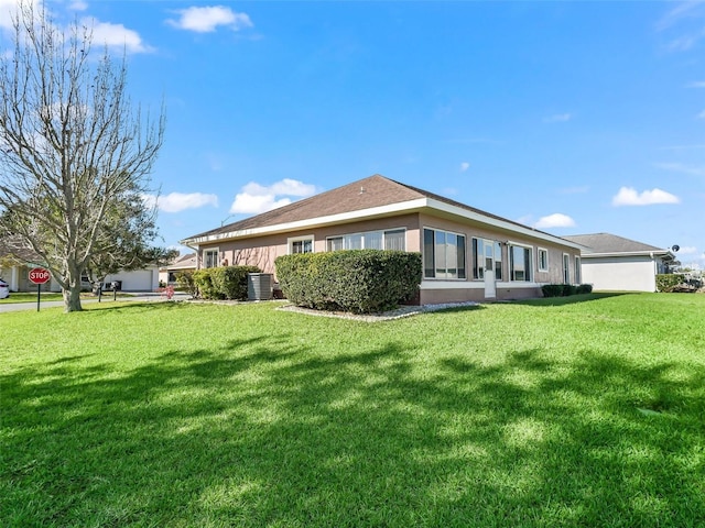 rear view of property with central AC unit, stucco siding, and a lawn