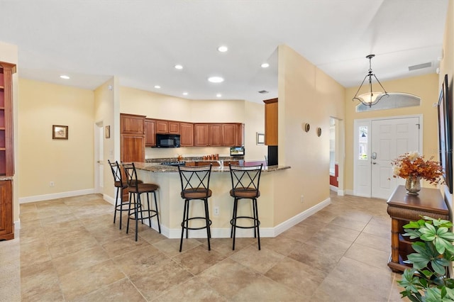 kitchen with visible vents, a breakfast bar, a peninsula, black microwave, and brown cabinets