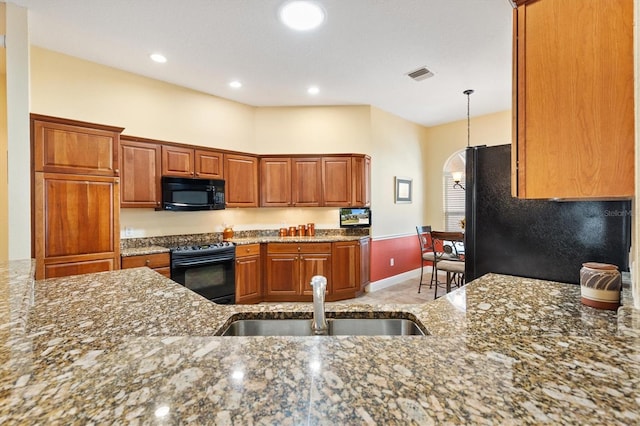 kitchen featuring a sink, brown cabinets, black appliances, and dark stone countertops