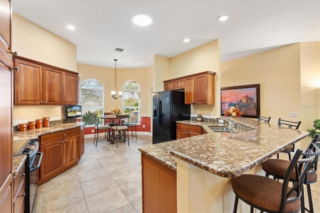 kitchen with a breakfast bar, a peninsula, brown cabinetry, black appliances, and a sink