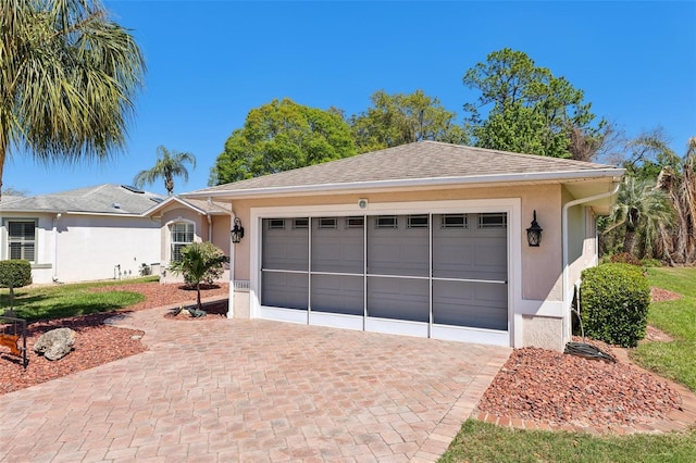 view of front facade featuring roof with shingles, decorative driveway, an attached garage, and stucco siding