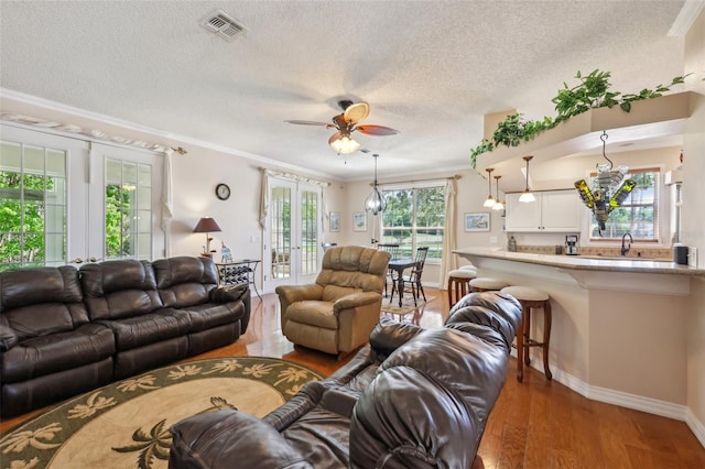 living room featuring a ceiling fan, wood finished floors, visible vents, french doors, and crown molding