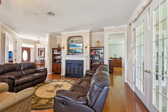 living room with wood finished floors, visible vents, a fireplace, ornamental molding, and a textured ceiling