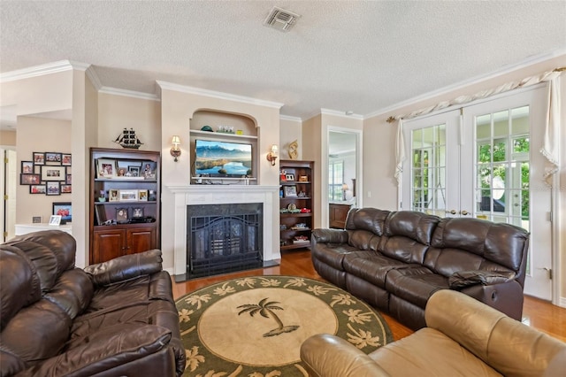 living area featuring wood finished floors, visible vents, a fireplace with flush hearth, a textured ceiling, and crown molding