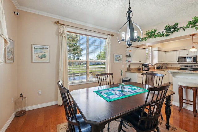 dining area with crown molding, light wood-style floors, baseboards, and a chandelier