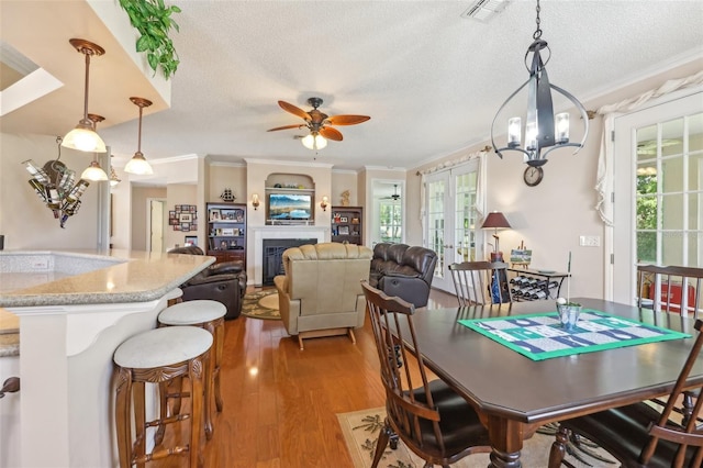 dining area with light wood finished floors, visible vents, french doors, a fireplace, and a textured ceiling