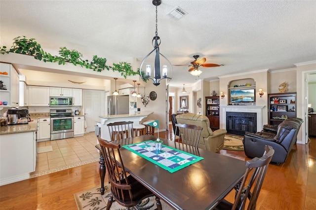 dining area featuring visible vents, a tile fireplace, light wood-style floors, a textured ceiling, and crown molding