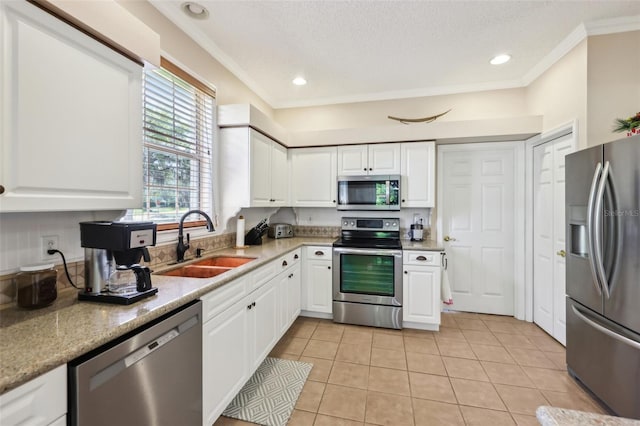 kitchen with light tile patterned floors, a sink, white cabinets, appliances with stainless steel finishes, and crown molding