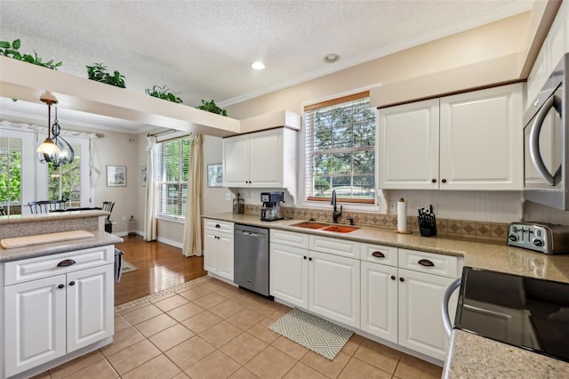 kitchen with pendant lighting, light countertops, ornamental molding, appliances with stainless steel finishes, and a sink