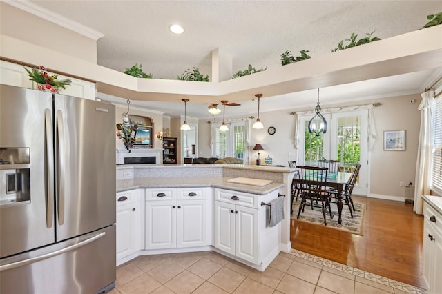 kitchen with light tile patterned floors, a peninsula, stainless steel fridge with ice dispenser, white cabinets, and crown molding