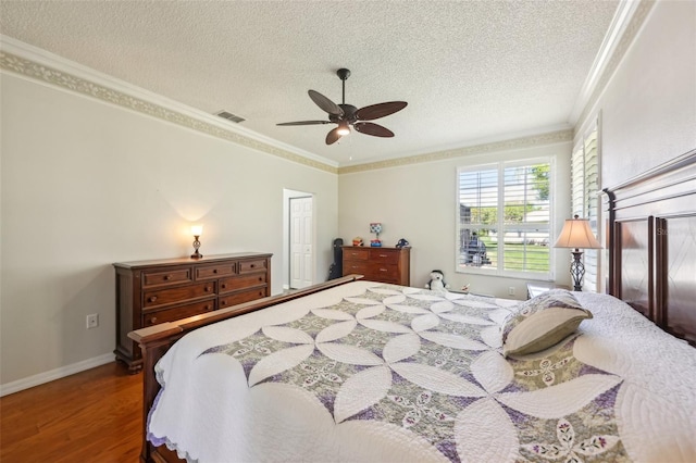 bedroom featuring wood finished floors, visible vents, ceiling fan, a textured ceiling, and crown molding