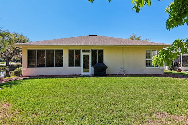 rear view of house with stucco siding, a lawn, and roof with shingles