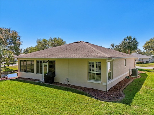 rear view of house with stucco siding, cooling unit, a yard, and roof with shingles