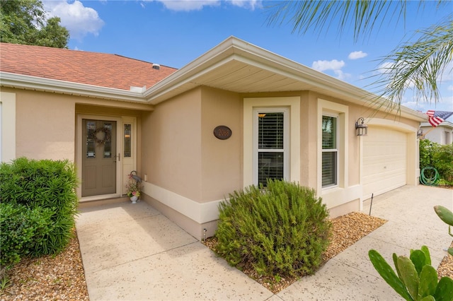 doorway to property with stucco siding, concrete driveway, an attached garage, and a shingled roof