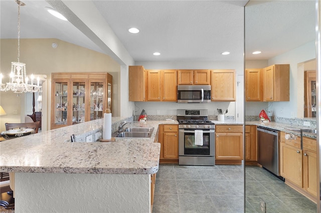 kitchen with light stone counters, an inviting chandelier, a peninsula, a sink, and appliances with stainless steel finishes