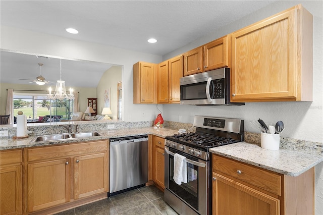 kitchen with light stone countertops, decorative light fixtures, ceiling fan with notable chandelier, stainless steel appliances, and a sink