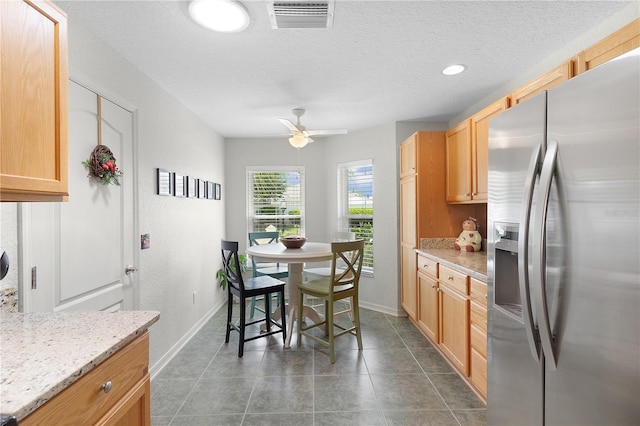 kitchen featuring visible vents, a ceiling fan, stainless steel refrigerator with ice dispenser, a textured ceiling, and baseboards