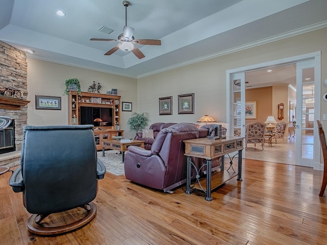 living area with a tray ceiling, visible vents, light wood-style floors, and a ceiling fan