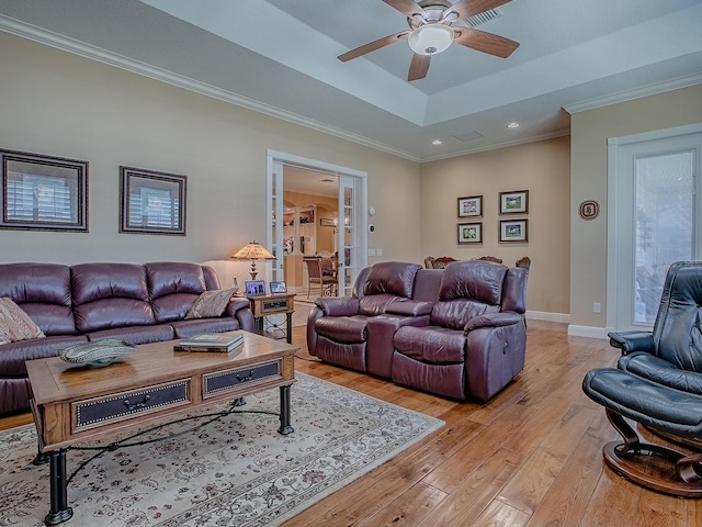 living room featuring crown molding, baseboards, light wood-style flooring, a raised ceiling, and a ceiling fan