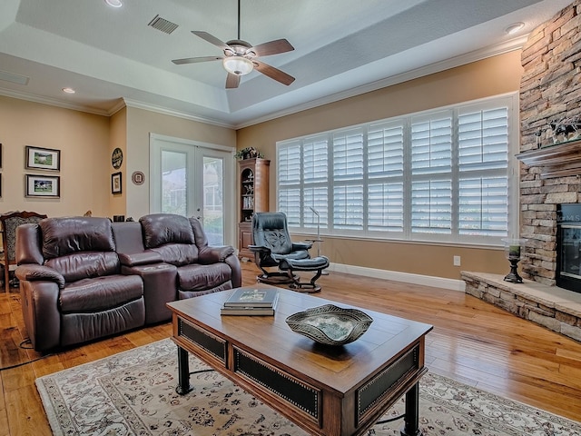 living area featuring visible vents, ornamental molding, light wood-style floors, a raised ceiling, and ceiling fan