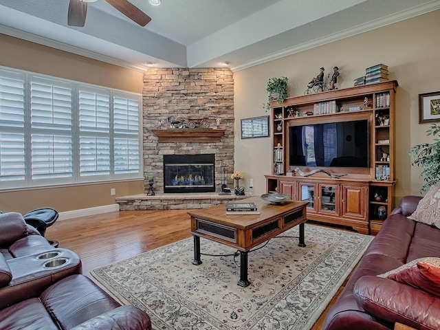 living room with crown molding, baseboards, ceiling fan, a stone fireplace, and wood finished floors